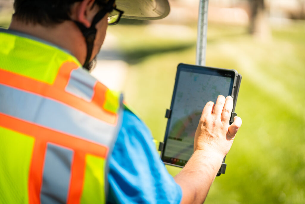 Close-up of a worker in safety gear using a mounted tablet outdoors to view a digital map.