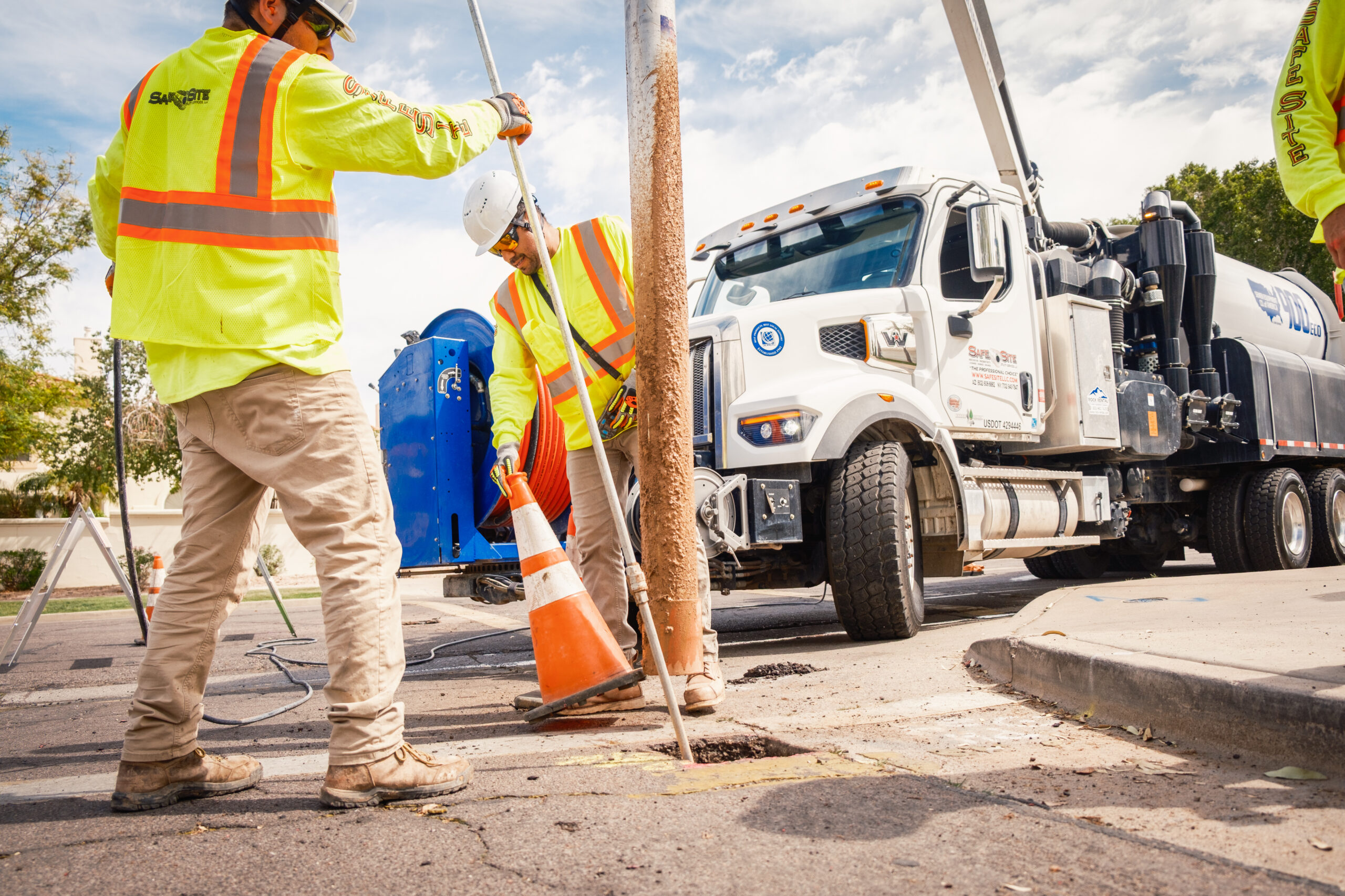 Two construction workers in high-visibility vests and hard hats working on a utility pole, with a white truck in the background.